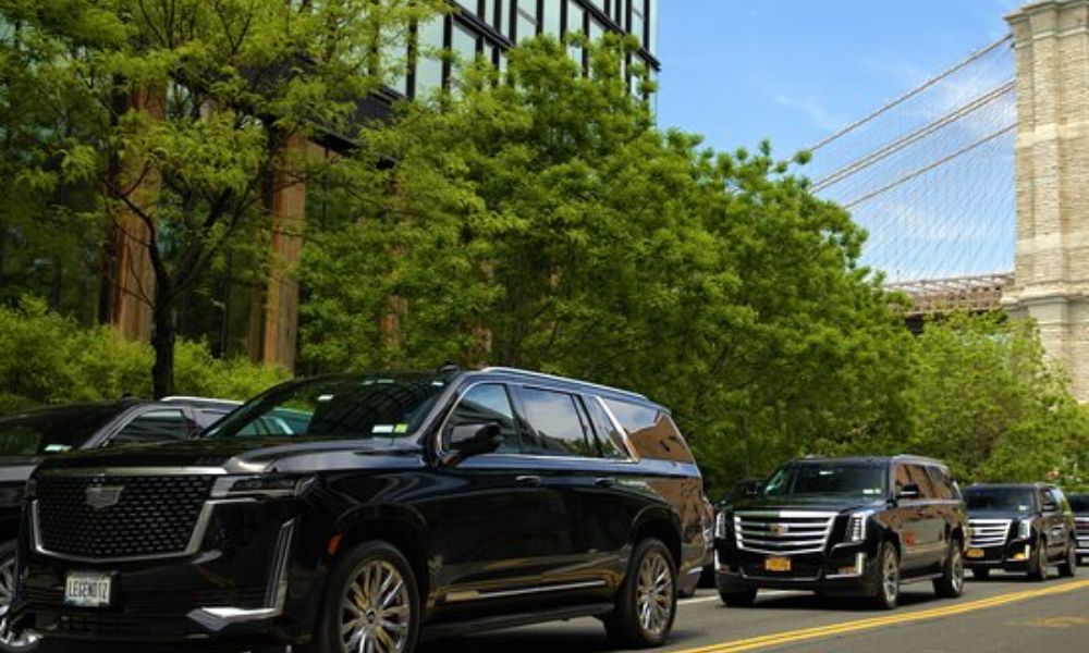 Black luxury SUVs lined up on city street near bridge.