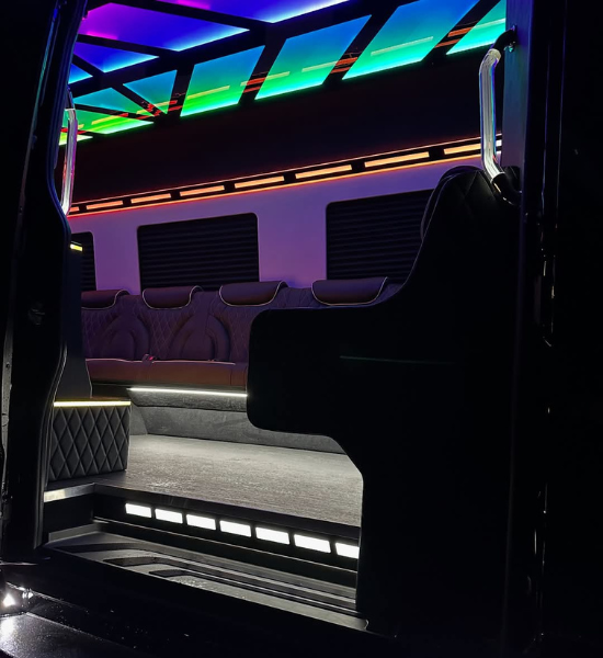 The interior of a luxury Sprinter van featuring quilted leather bench seating and vibrant, multi-colored neon LED lighting on the ceiling and walls.