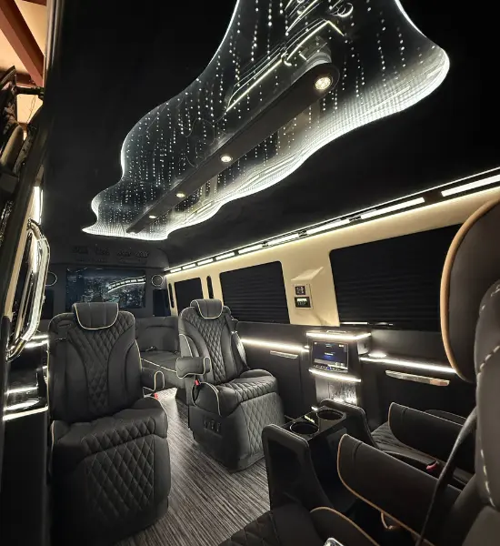 Luxurious interior of a black Sprinter van featuring quilted leather captain’s chairs, custom starlight ceiling lighting, and premium entertainment screens Luxurious interior of a black Sprinter van featuring quilted leather captain's chairs, custom starlight ceiling lighting, and premium entertainment screens