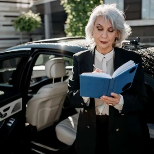 Professional chauffeur in business attire reviewing a scheduling book next to a luxury black sedan for Miami to Fort Myers car service