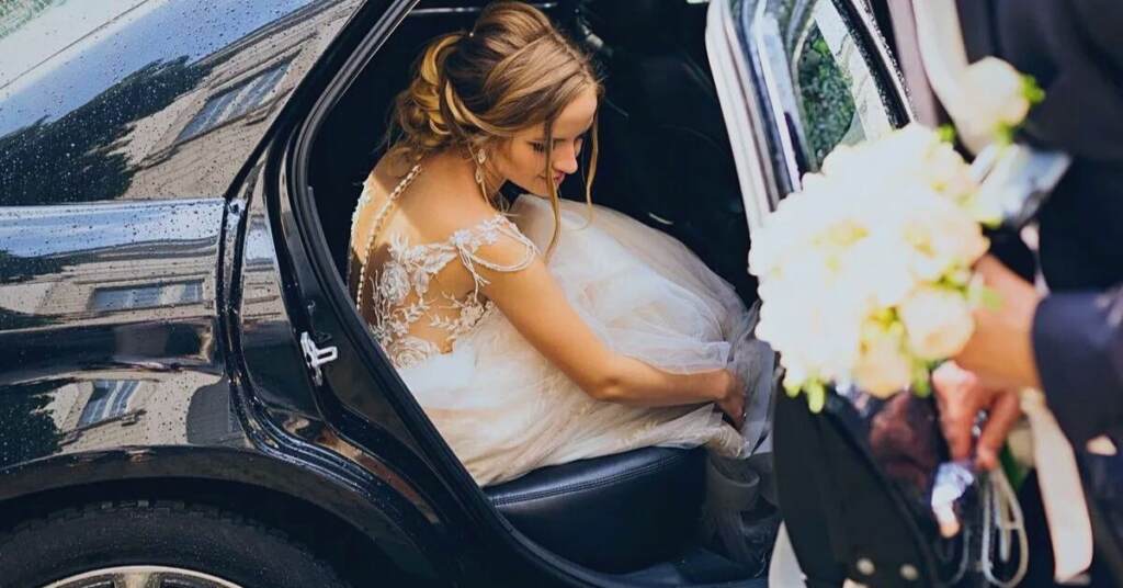 bride entering black wedding car with floral bouquet